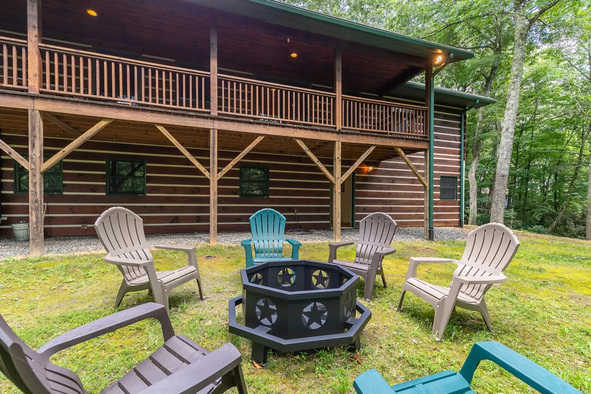An inviting outdoor space featuring a fire pit surrounded by Adirondack chairs, set on a flat paved area with lush trees creating a cozy, private ambiance. The arrangement encourages gathering, conversation, and relaxation in nature.
