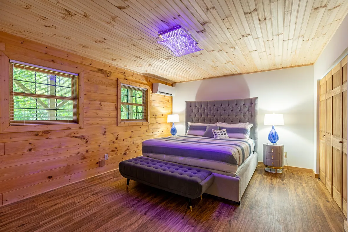 An elegant bedroom with a tufted headboard, blue accent lamps, and rich wooden flooring. The space is bathed in natural light, evoking serenity and calm—a perfect retreat for quiet moments or restful sleep.