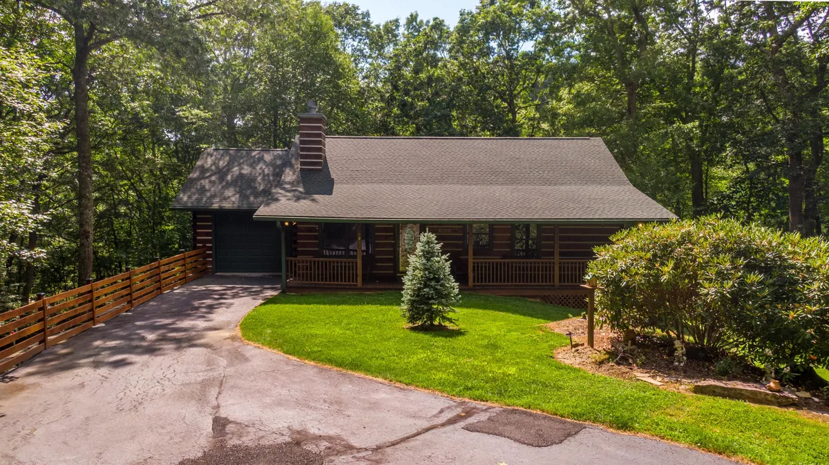 A welcoming view of the log cabin’s exterior with a lush, green lawn stretching in front, a spacious front porch, and trees surrounding the property. The expansive lawn is perfect for pets and outdoor play.