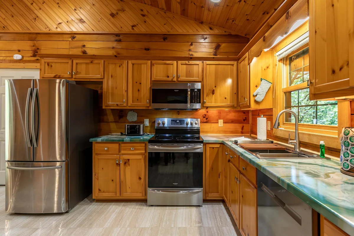 A bright and inviting kitchen scene, showcasing a stainless steel refrigerator, stove, microwave, and kitchen sink—all surrounded by ample cabinetry. The layout encourages meal preparation and social interaction, providing both function and a welcoming atmosphere.